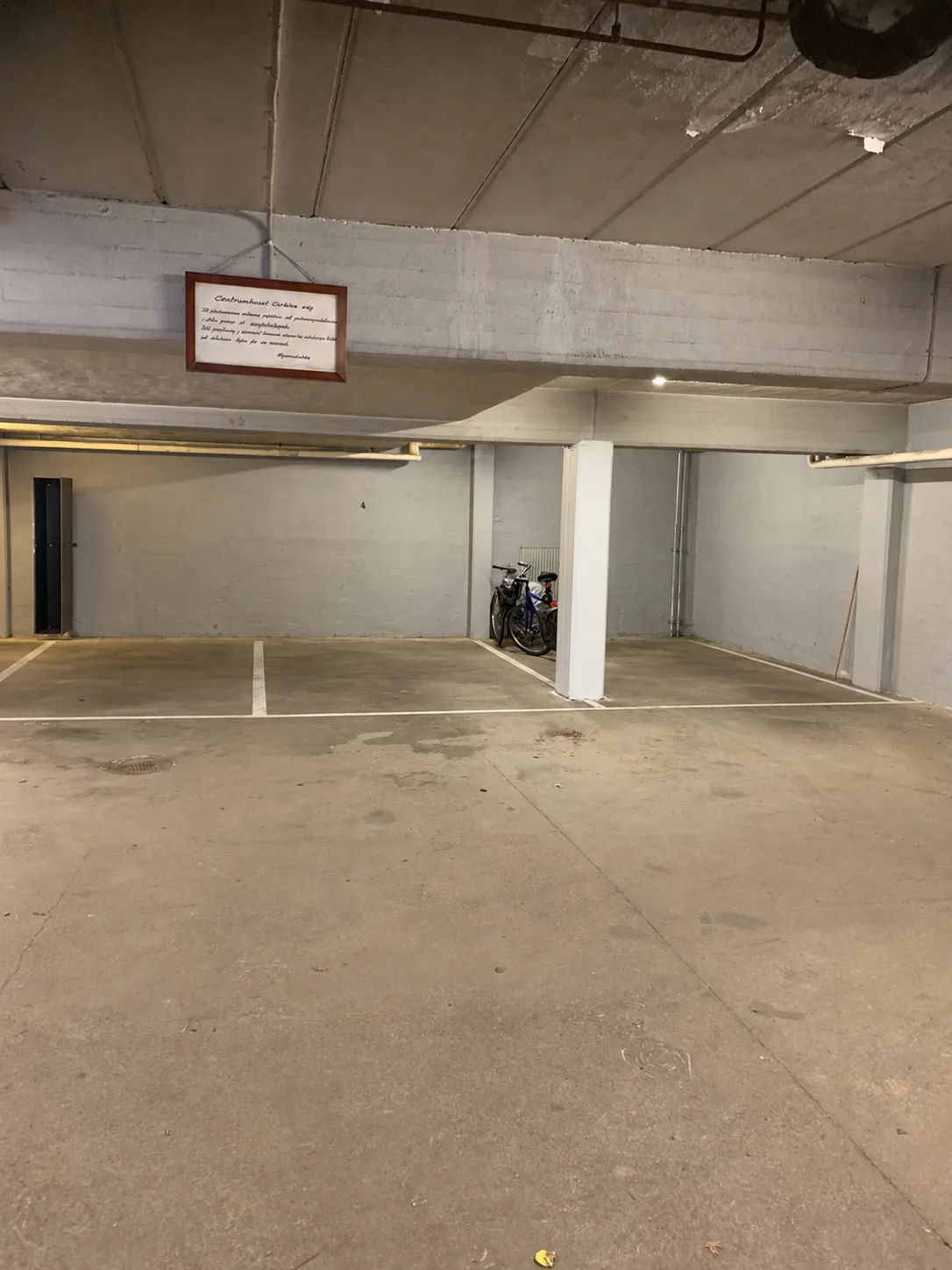 Parkeringsgarage med markerade parkeringsrutor, vit pelare, cyklar och hängande informationsskylt
