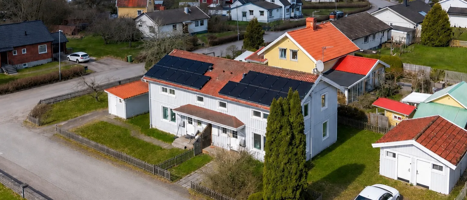 Drönarvy över Vintergatan 4A–B med ljusgrå träpanel, tegelrött tak och solceller i ett lugnt villakvarter