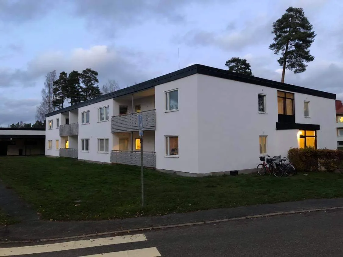 Fastigheten vid Carléns väg 14 i skymning med tända fönster, balkonger och cyklar vid gaveln