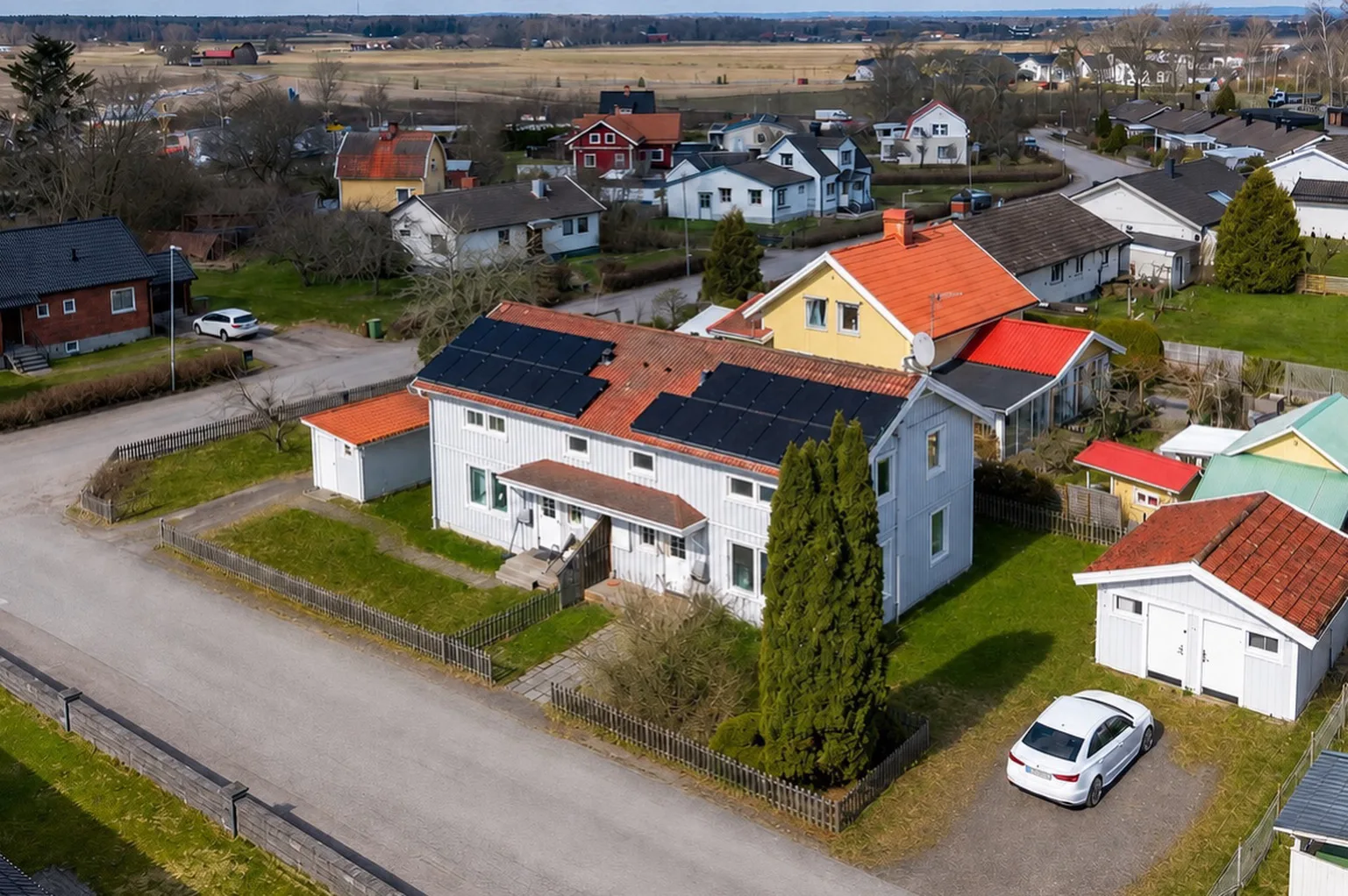 Drönarvy över Vintergatan 4A–B med ljusgrå träpanel, tegelrött tak, solceller och gräsmattor i ett lugnt villakvarter