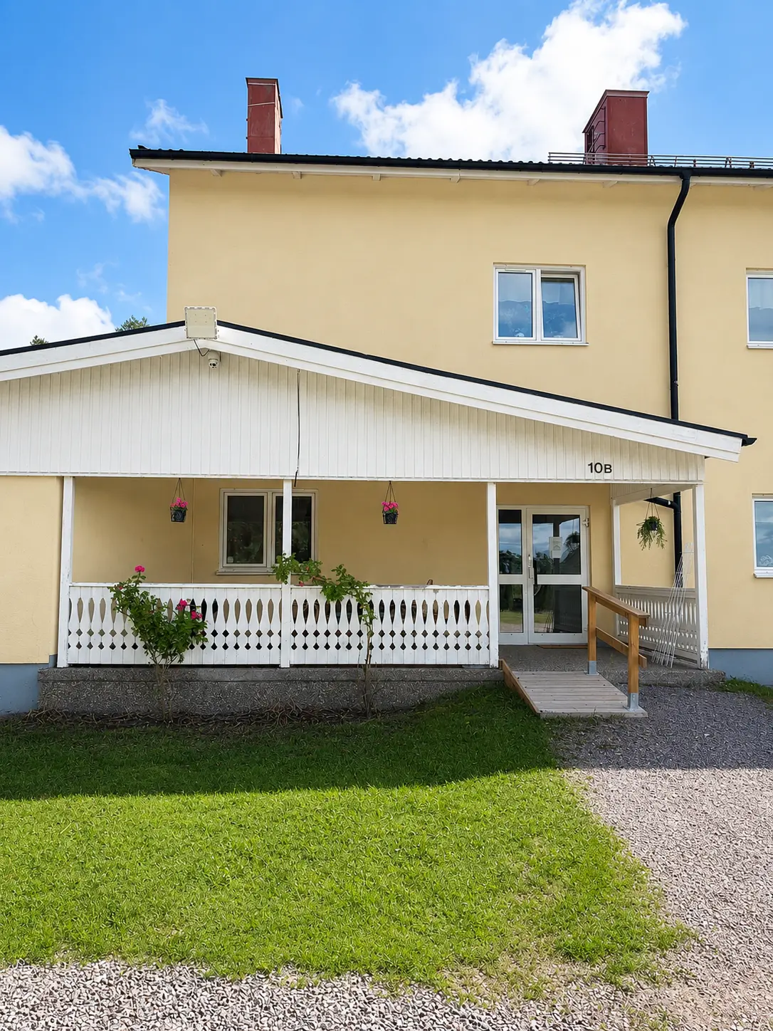 Entrén till Norra Storgatan 10A–B med övertäckt veranda, blomampel och tillgänglighetsanpassad ramp